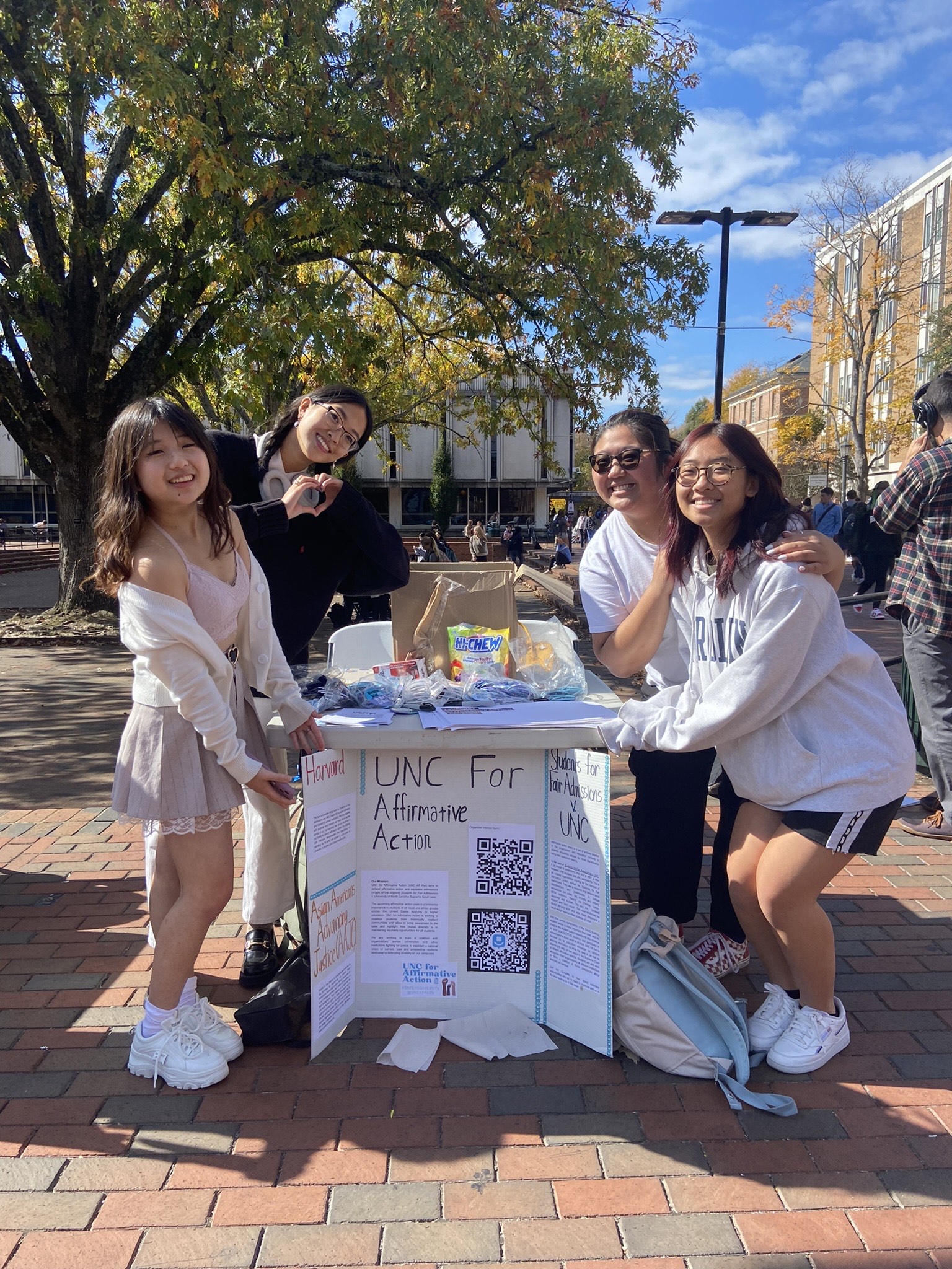 Student activists pose around a table and trifold board on a sunny day.