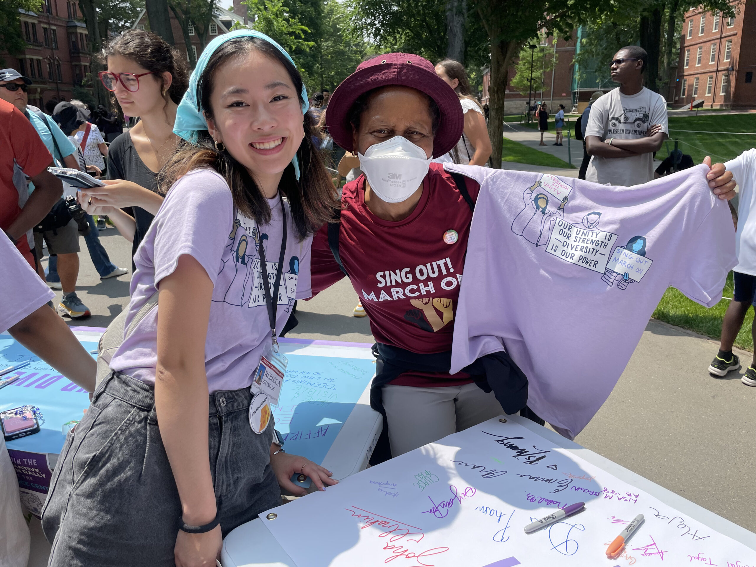 A student in a purple T-shirt poses with an alum in a red shirt behind a table with markers on top.