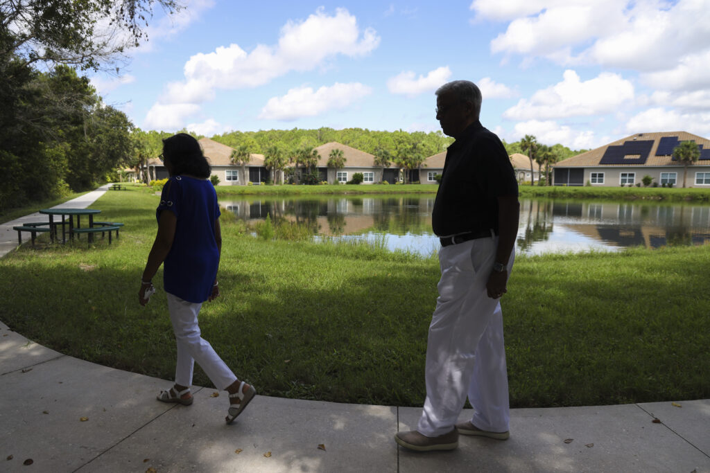 (Left) Puspa Tijoriwal, 72, and (right) Suresh Tijoriwal, 74, walk along a walking trail with homes in the background at Anand Vihar, a 55-plus residential community located in Wesley Chapel. July 16, 2025.